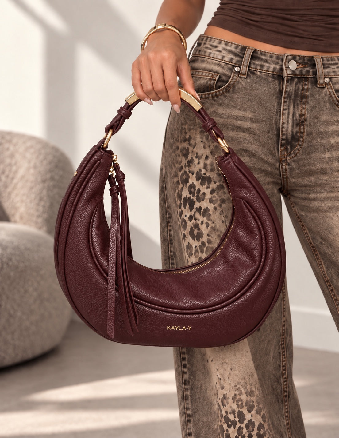 Borsa Ella bordeaux a mezzaluna con dettagli dorati, tenuta a mano dalla modella