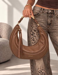 Borsa Ella cuoio a mezzaluna con dettagli dorati, tenuta a mano dalla modella